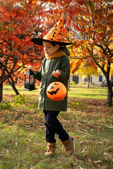 Happy Halloween child holding a pumpkin candy bucket while standing in the autumn forest