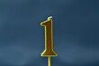 close up on gold number one birthday candle on a dark background.
