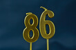 close up on gold number eighty-sixth candle on a dark background.
