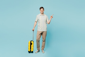 Poster - Full body traveler man wear shirt casual clothes hold bag suitcase point aside isolated on plain blue background. Tourist travel abroad in free spare time rest getaway Air flight trip journey concept