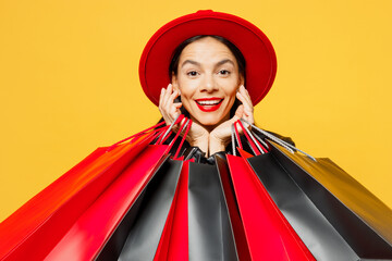 Wall Mural - Close up young smiling cheerful fun happy woman wearing casual clothes red hat holding shopping paper package bags looking camera isolated on plain yellow background Black Friday sale buy day concept