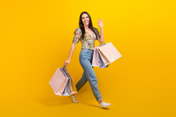 Poster - Full length photo of pretty girl dressed flower print blouse hold new clothes say hello waving arm isolated on yellow color background