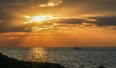 Sticker - A small fishing boat moored in the middle of the sea during sunset in Thailand.