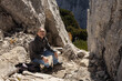 © Guzel - Gray-haired long-haired man sitting in a rock crevice on the background of a cliff, active lifestyle concept, Austria
