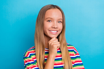 Poster - Portrait of toothy beaming schoolgirl with long hairstyle wear colorful t-shirt smiling fingers on chin isolated on blue color background