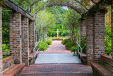 Fototapeta Na drzwi - A long red brick footpath with a metal awning covered with lush green plants and trees with a gold statue at the end of the footpath at New Orleans Botanical Garden in New Orleans Louisiana USA