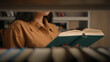 © Yuliia - Unrecognizable woman reading book in university library near bookcase smart female girl college student teacher read textbook literature prepare for exam studying homework view through bookshelf books