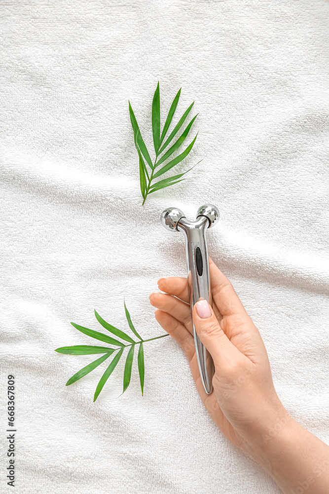 Female hand with metal face massage roller on white towel