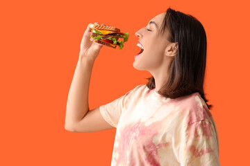 Wall Mural - Beautiful young woman eating tasty sandwich on orange background