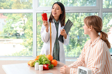 Canvas Print - Female Asian nutritionist with healthy food and patient in office