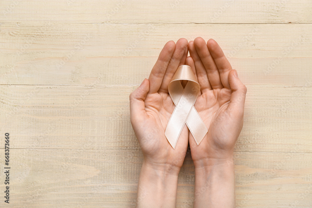 Woman with beige ribbon on light wooden background. Uterine cancer awareness concept