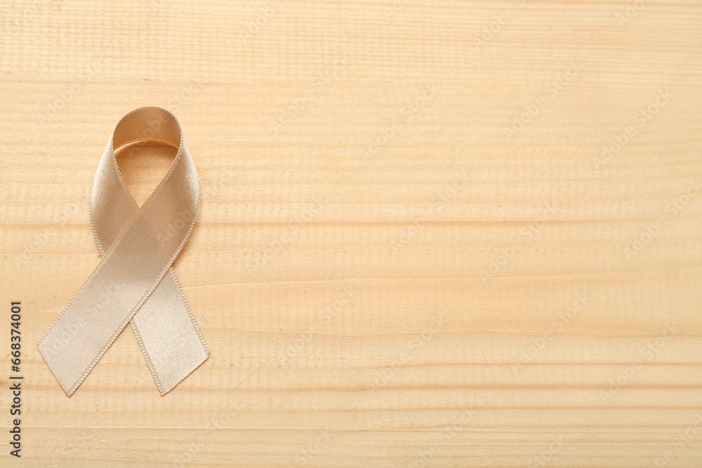 Beige ribbon on light wooden background. Uterine cancer awareness concept