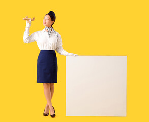 Wall Mural - Beautiful Asian stewardess with blank poster on yellow background