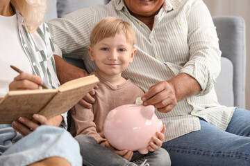 Canvas Print - Little boy with his grandparents putting coin in piggy bank at home