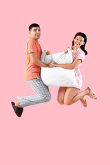 Wall Mural - Young couple with pillow jumping on pink background