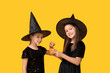 © Pixel-Shot - Cute little girls dressed for Halloween as witches with tasty candies on yellow background