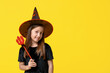 © Pixel-Shot - Cute little girl dressed for Halloween as witch with red devil pitchfork on yellow background