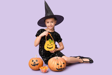 Wall Mural - Cute little girl dressed for Halloween as witch with pumpkins, bag and candies sitting on purple background