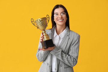 Wall Mural - Young businesswoman with gold cup on yellow background