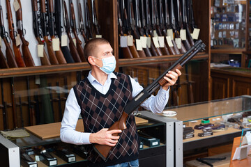 Wall Mural - Gun shop salesman in protective face mask demonstrates a pump action shotgun