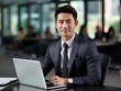 © DigitalArt - A confident young man in a sharp suit sits at a desk with a laptop, set against the backdrop of a modern office with colleagues in the background.