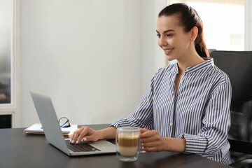 Wall Mural - Happy woman using modern laptop at black desk in office