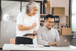 © Phushutter - An older mature woman shows something to asian man on a laptop. They smile and work together in an office. They look happy and focused.