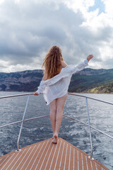 Woman on a yacht. Happy model in a swimsuit posing on a yacht against a blue sky with clouds and mountains