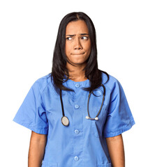 Young Filipina nurse posed in studio confused, feels doubtful and unsure.