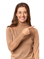 Wall Mural - Middle-aged woman portrait in studio setting smiling and pointing aside, showing something at blank space.