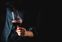 woman hands pouring red wine into a glass from a bottle on black background
