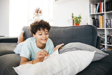 Ten years old girl lying on a sofa and reading a book in a living room.