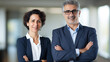 © BlazingDesigns - Portrait of smiling mature businessman and mature business woman standing arms crossed in office. Two diverse colleagues planning and collaboration.