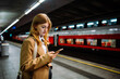 © Big Shot Theory - Young woman stands at a subway station and looks at her mobile phone