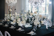 Table setting, setup. Banquet decoration composition flowers, candles in hall restaurant. Table covered black tablecloth. Luxury wedding reception. Trendy decor large chandelier for a birthday party.
