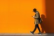 © Dina - millennial guy with hat texting on mobile phone walking past yellow orange wall