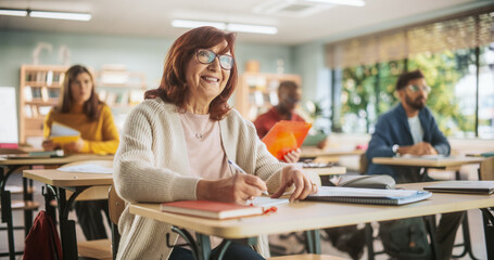 Leinwandbilder - Portrait of a Happy Senior Woman Taking a Course in an International Adult Education Center. Focused Elderly Female Wearing Glasses, Sitting Behind a Desk, and Writing Down Notes in a Notebook.