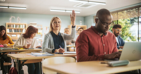 Fototapete - Diverse Mature Students Learning in Classroom, Using Laptops and Writing in Notebooks. Female Raising Hand and Asking Teacher a Question During a Lecture in Adult Education Course in School