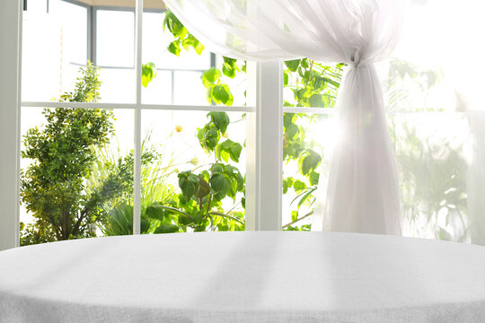 empty table with white tablecloth against window indoors. space for design