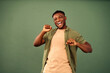 Expressing happiness. Carefree millennial guy wearing unbuttoned khaki shirt joyfully dancing with hands over green background. African american man dynamically moving body while feeling rhythm.