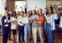 Portrait Of Diverse Excited Happy Business People Standing In Office Applauding And Looking Cheerful At The Camera. Group Of Coworkers Men And Women Smiling Indoors. Team Work Concept.
