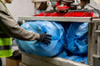 Close-up shot of male hands in gloves loading large garbage bags into special garbage compactor machine for waste disposal