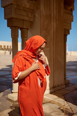 Dynamic portrait of a stylish woman in Islamic ethnic attire, looking down, standing between marble columns of a mosque