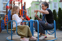 Two Generations, A Senior And A Young Woman, United By The Joy Of Sign Language Communication, Celebrating Their Intergenerational Friendship In A Colorful Park Setting