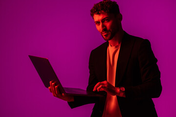 Work and play online. Happy man holding laptop and typing in neon light, copy space