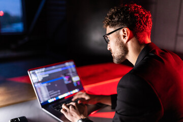 young smart man mobile developer writes program code on a computer, programmer work in home office.