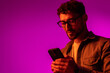 © F8  \ Suport Ukraine - Side view of astonished surprised man in shirt using online service on mobile phone on neon light background.