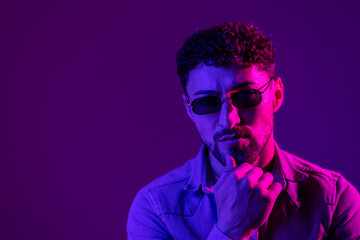 Studio shot of handsome young man in stylish sunglasses isolated on g pink background in neon light.