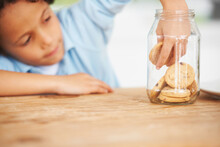 Hands, Cookie Jar And Boy Child By The Kitchen Counter Eating A Sweet Snack Or Treat At Home. Smile, Dessert And Cute Hungry Young Kid Enjoying Biscuits By A Wooden Table In A Modern Family House.