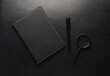 Black leather notebook with pen and magnifying glass on leather surface.